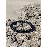 Bracelet Obsidienne Argentée en perles rondes sur rochers côtiers, bijou sobre aux reflets fumés pour transformation intérieure et recentrage.