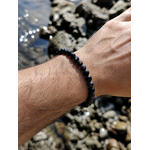 Bracelet Obsidienne Argentée porté au poignet près des rochers bretons, bijou en pierre naturelle associé à l’ancrage et à la stabilité émotionnelle.