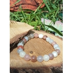Bracelet Pierre de Lune beige multicolore sur tranche de bois au soleil, bijou naturel aux tons pêche, blanc et gris pour douceur lunaire.