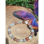 Bracelet en pierre de lune beige multicolore posé sur bois avec papillon décoratif, nuances naturelles tendres pour harmonie et écoute intérieure.