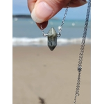 Pendentif pointe Labradorite tenu devant la mer, chaîne argentée en acier inoxydable et pierre naturelle aux reflets discrets.