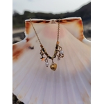Collier doré à breloques célestes suspendu sur coquillage blanc, cœur central, lune, étoile et perles nacrées en bord de mer.
