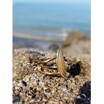 Bague ovale dorée vue de profil sur roche coquillée, anneau acier inoxydable et motif travaillé face au bord de mer.