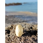 Bague dorée en acier inoxydable sur décor marin, plateau ovale texturé aux reflets lumineux et détails concentriques.