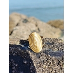 Bague dorée texturée posée sur rocher côtier, plateau ovale en relief et finition brillante pour une touche bohème chic.