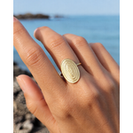 Bague dorée ovale portée au doigt face à la mer, acier inoxydable texturé au motif relief élégant et solaire.