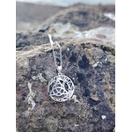 Pendentif Triquetra Lune en argent 925 sur rocher en bord de mer, symbole celtique ajouré et reflets lumineux.