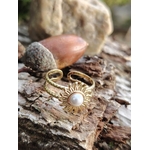 Bague dorée ajustable Soleil avec cabochon blanc nacré posée sur écorce et glands, bijou lumineux en décor naturel breton.