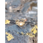 Bague Soleil dorée sur roche sombre avec lichens jaunes, centre nacré et rendu éclatant au bord de mer.