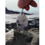Pendentif Péristérite tenu devant les rochers et la mer en Bretagne, pierre lunaire blanche aux taches naturelles.