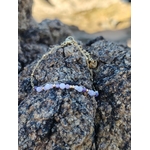 Bracelet Améthyste facettée sur rocher côtier breton, chaîne fine dorée et breloques pour équilibre émotionnel.