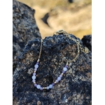 Bracelet Améthyste facettée doré posé sur roche en bord de mer breton, perles violettes et breloques pour sérénité.