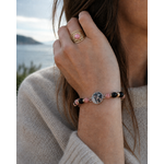 Bracelet rose, noir et doré porté au poignet avec bague assortie, face à la mer en Bretagne, élégance douce et harmonie émotionnelle.