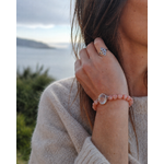 Bracelet en perles rose pâle avec cabochon central argenté porté en bord de mer en Bretagne, accompagné d’une bague nœud de sorcière pour douceur et protection.