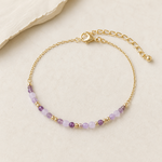Bracelet améthyste facetté 3 mm sur chaîne dorée, perles lilas et parme avec petits intercalaires dorés sur fond beige élégant.