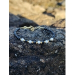 Bracelet Tourmaline Noire facettée 2 mm et cuivre plaqué or posé sur roche naturelle, bijou fin noir, blanc et doré pour ancrage et stabilité intérieure.