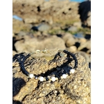 Bracelet fin en tourmaline noire facettée avec perles blanches et détails dorés, photographié sur rocher en lumière naturelle, style délicat et protecteur.