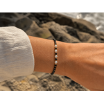 Bracelet Tourmaline Noire facettée 2 mm porté au poignet près de la mer sur rochers, perles noires, blanches et dorées pour protection et élégance discrète.