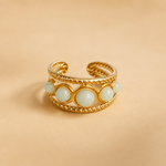 Bague dorée ajustable multi Amazonite sur fond beige doux, monture ajourée et cabochons bleu-vert pour équilibre émotionnel.