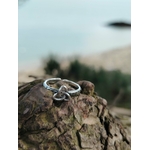 Bague argentée Triquetra posée sur tronc avec mer floue en arrière-plan, bijou ajustable évoquant unité, cycles et équilibre intérieur.
