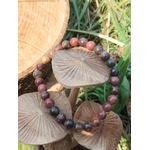 Bracelet Jaspe Polychrome présenté sur des champignons décoratifs en bois avec herbes autour, perles rouge brun et noires, pour retour à soi et équilibre.