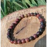 Bracelet Jaspe Polychrome posé sur une tranche de bois en extérieur, perles aux teintes bordeaux, ocre et sombres, pour force tranquille et ancrage.