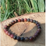 Bracelet Jaspe Polychrome photographié sur une tranche de bois avec herbes en arrière-plan, perles rouges, brunes et noires, pour protection et ancrage profond.