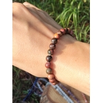 Bracelet Jaspe Polychrome porté au poignet en lumière naturelle, perles aux tons terreux et marbrés sur fond végétal, pour sérénité et confiance en soi.