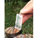 Pendentif Calcite Optique tenu à la main en extérieur, pierre transparente sur cordon noir avec fond végétal pour clarté et intuition.