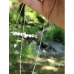 Détail du collier Labradorite tenu à la main, perles claires et reflets froids dans une ambiance boisée.