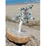 Création Magic Gaïa arbre en larimar sur rondin naturel, photographié sur rocher avec plage et mer bretonne en arrière-plan.