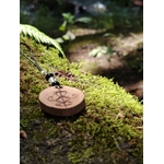 Accessoire Magic Gaïa en bois pyrogravé avec sigil protecteur, tourmaline noire et cristal de roche parmi la mousse.
