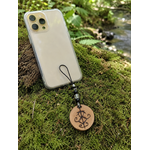 Smartphone avec talisman Magic Gaïa suspendu, bois naturel pyrogravé et pierres associées à l’ancrage protecteur.