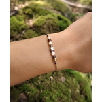 Bracelet étoile dorée porté au poignet en lumière naturelle, cordon noir ajustable et petites perles lumineuses aux tons doux.
