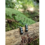 Boucles d’oreilles hématite création Magic Gaïa posées sur branche, mousse et fougère en décor naturel, stabilité intérieure.