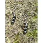 Boucles d’oreilles hématite création Magic Gaïa sur écorce avec mousse verte, reflets brillants, ancrage profond.