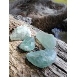 Fluorite verte brute naturelle posée sur un tronc de bois en forêt, pierres de lithothérapie aux nuances vert translucide