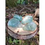 Fluorite verte brute naturelle sur rondin de bois en sous-bois, pierres de lithothérapie vert translucide pour clarté mentale et apaisement