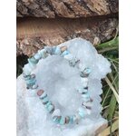 Bracelet larimar baroque posé sur tissu blanc duveteux avec bois brut et feuillage, pierres bleu ciel marbrées pour réconfort affectif et détente mentale