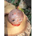 Sphère en Pierre de Soleil naturelle (héliolite) sur socle bois et rondin, reflets nacrés orangés, fond végétal — symbole de joie, d’optimisme et d’énergie positive.
