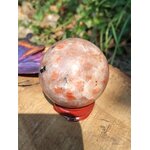 Sphère en Pierre de Soleil naturelle (héliolite) sur socle en bois, reflets nacrés orangés, posée sur planche de bois — symbole de joie et d’optimisme.