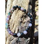 Bracelet en tourmaline multicolore posé sur bois flotté, perles roses, violettes, bleutées et noires pour recentrage et force calme