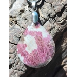 Gros plan sur pendentif goutte en tourmaline rose avec bélière en acier inoxydable, photographié sur écorce, bijou en pierre naturelle évoquant la délicatesse, la paix émotionnelle et le réconfort.