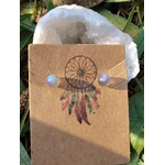 Puces d’oreilles en labradorite bleue, présentés sur un support kraft à motif attrape-rêves devant une géode blanche ; pierre d’intuition, de protection énergétique et d’harmonie intérieure.