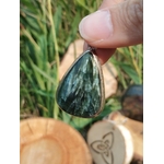 Bijou en séraphinite véritable cabochon goutte en argent 925, présenté en main devant herbes et rondins, pierre naturelle liée au recentrage, à l’écoute de soi et à l’harmonie intérieure.