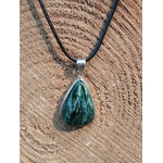Pendentif en séraphinite véritable à texture fibreuse avec bélière argent, posé sur bois brut en extérieur, bijou en pierre naturelle évoquant la douceur, la paix émotionnelle et la présence à soi.