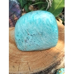 Forme libre amazonite bleu-vert, texture fibreuse, posé sur tranche de bois; arrière-plan nature — apaisement et communication douce.