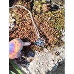 Pendentif graine de vie en argent 925 posé sur mousse et rocher, symbole de géométrie sacrée dans un décor naturel
