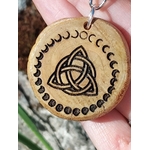 Gros plan porte-clés en bois gravé triquetra celtique et phases de lune, tenu entre les doigts