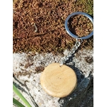 Dos du porte-clés en bois rond, surface lisse, anneau métallique sur rocher et mousse.